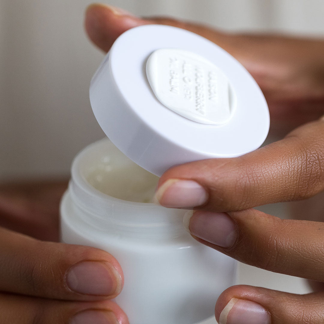 Hands openning All-Over Oil Balm moisturizer jar to show texture